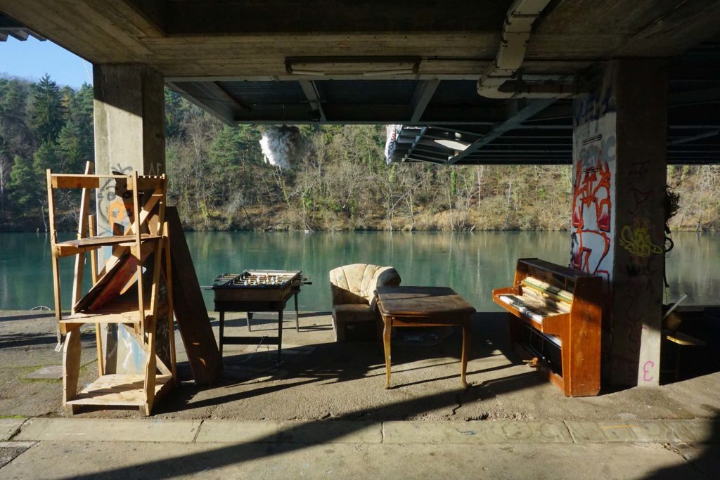 Bord de fleuve, quai avec un fauteuil, un vieux baby-foot et un piano laissés à l'abandon.